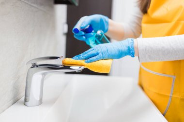 Kadın ellerine koruyucu eldivenler giydirin. Temizlik ve banyo musluğunu temizleyin. Kumaş ve dezenfektanla temizleyin. Hijyen kavramı.