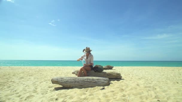 Туристка с рюкзаком пьет воду на пляже — стоковое видео
