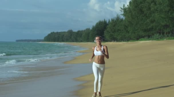 Flicka kör på stranden med hörlurar — Stockvideo