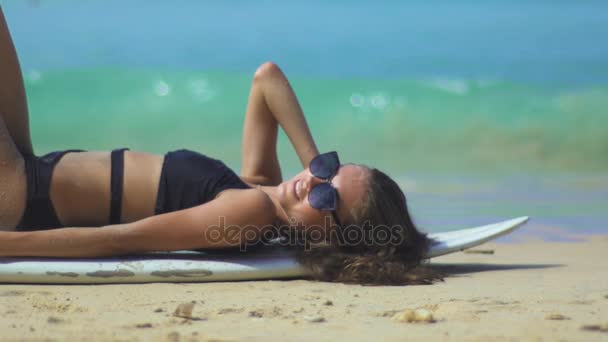 Chica acostada en la tabla de surf mientras toma el sol — Vídeo de stock