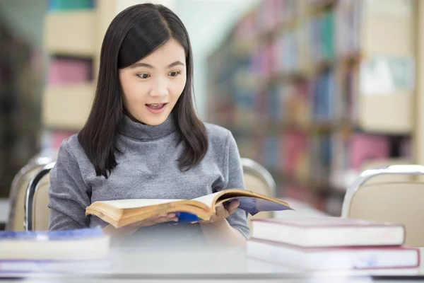 Surprised woman reading a book in the library — Stock Photo, Image