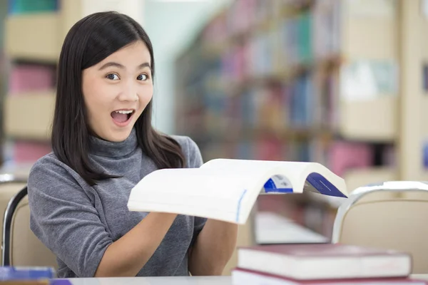 Surprised woman reading a book in the library — Stock Photo, Image