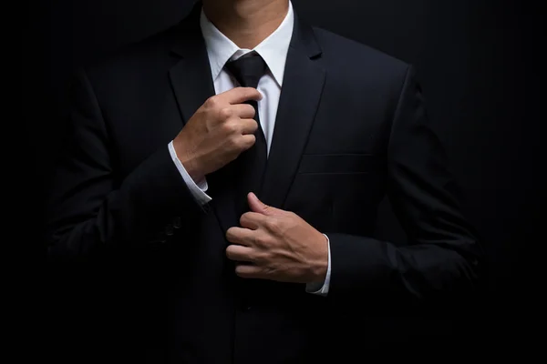 Man in black suit and adjusting his necktie — Stock Photo, Image