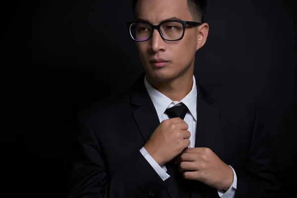 Man in black suit and adjusting his necktie