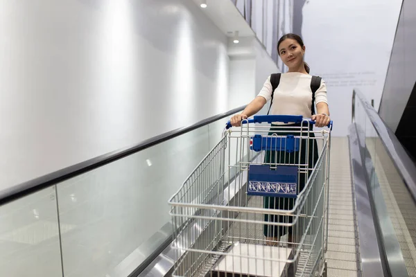 Yürüyen merdivende alışveriş arabası olan bir kadın. — Stok fotoğraf