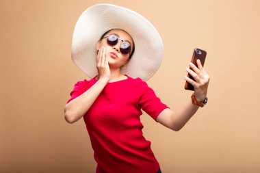 Şapka takan ve güneş gözlüğü takan kadın çantadan izole edilmiş akıllı telefon kullanıyor.