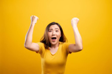 Mutlu kadın sarı arka planda izole edilmiş kazanan bir jest yapar.