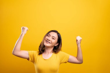 Mutlu kadın sarı arka planda izole edilmiş kazanan bir jest yapar.