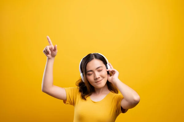 Femme avec écouteurs écoutant de la musique sur fond jaune isolé — Photo