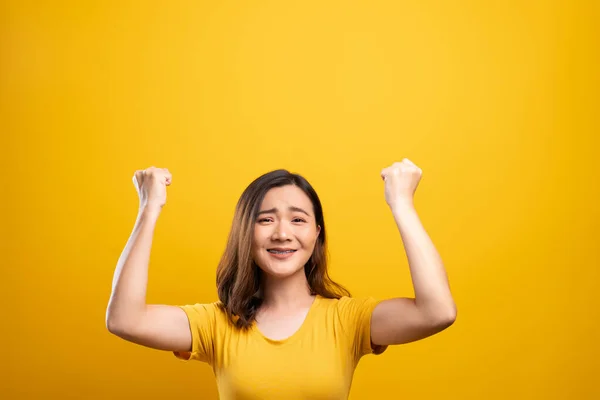 Happy woman make winning gesture isolated over yellow background — Stock Photo, Image
