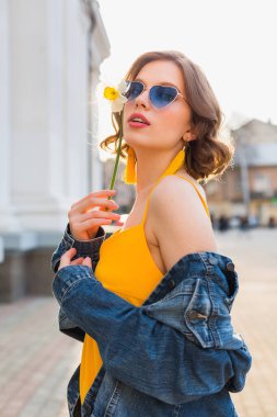Güzel, stil sahibi, sarı elbiseli, kot ceketli, modaya uygun kıyafetler giyen, bahar moda trendi, güneşli, mavi güneş gözlüklü, sokak modası, hippi tarzı, moda aksesuarları giyen seksi bir kadın.
