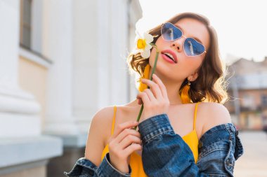 Güzel, stil sahibi, sarı elbiseli, kot ceketli, modaya uygun kıyafetler giyen, bahar moda trendi, güneşli, mavi güneş gözlüklü, sokak modası, hippi tarzı, moda aksesuarları giyen seksi bir kadın.