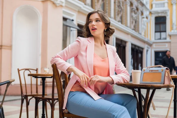 ピンクのジャケットの夏のスタイルの傾向でテーブルドリンクコーヒーに座ってスタイリッシュな官能的な女性の肖像画 青のハンドバッグ アクセサリー ストリートスタイル 女性のファッション — ストック写真