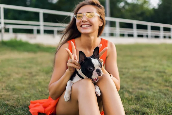 夏の公園で草の上に座っている幸せな女性の肖像画 ボストンのテリア犬を保持し 面白い顔の表情 笑顔肯定的な気分 ペットと遊ぶ 楽しみを持っている — ストック写真