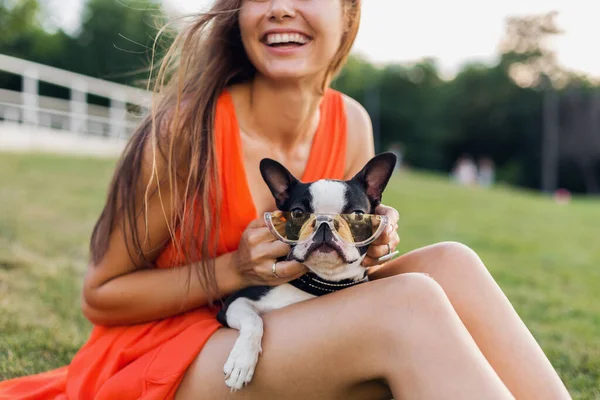ボストン テリアを持つ夏の公園で草の上に座っている女性のクローズアップ スタイリッシュなサングラスを身に着けている面白い犬 ペットと遊ぶ女の子 楽しい 夏のファッショントレンドを持っている — ストック写真