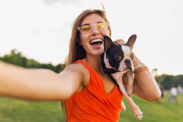 公園で犬と遊ぶ楽しいオレンジドレスの若い幸せな笑顔の女性 夏のスタイル 陽気な気分 カメラで自撮り写真を作る — ストック写真