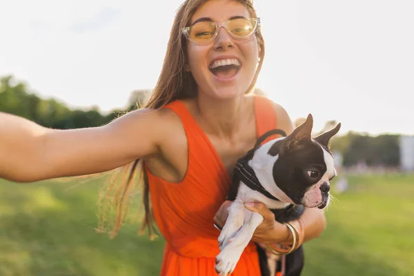 公園で犬と遊ぶ楽しいオレンジドレスの若い幸せな笑顔の女性 夏のスタイル 陽気な気分 カメラで自撮り写真を作る — ストック写真
