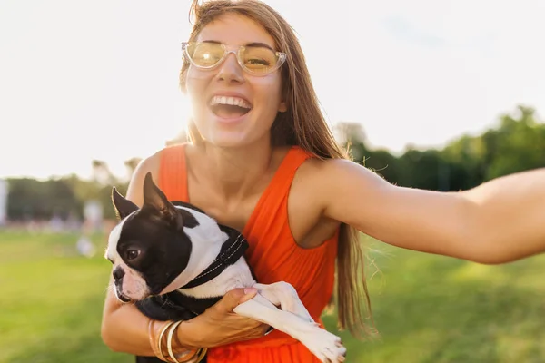 公園で犬と遊ぶ楽しいオレンジドレスの若い幸せな笑顔の女性 夏のスタイル 陽気な気分 カメラで自撮り写真を作る — ストック写真