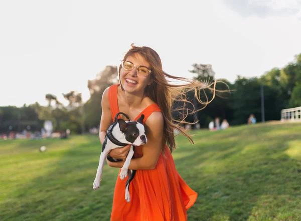 公園で犬と遊ぶ楽しいオレンジのドレスの若い幸せな笑顔の女性 夏のスタイル 陽気な気分 — ストック写真
