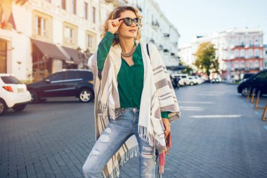 Mutlu pozitif kadın portresi samimi gülümsüyor, bahar moda tarzı, yeşil bluz, şapka, çanta, pelerin, güneş gözlüğü takıyor