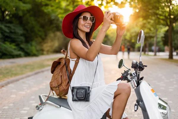 白いドレスを着た夏のスタイルの服装でバイクに乗っている魅力的な笑顔の女性と休暇中に旅行する赤い帽子 ヴィンテージフォトカメラで写真を撮る — ストック写真
