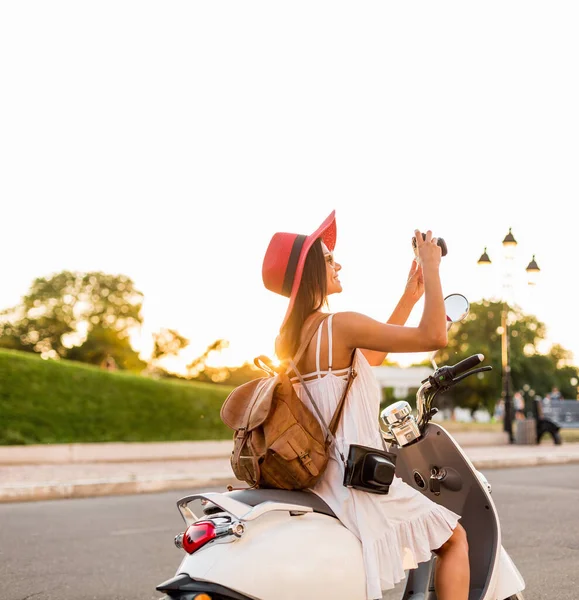 ストリートバイクに乗って魅力的な女性 夏休みのスタイル 楽しみを持っています スタイリッシュな衣装 ヴィンテージ写真カメラで写真を撮る 革のバックパックを身に着けています — ストック写真