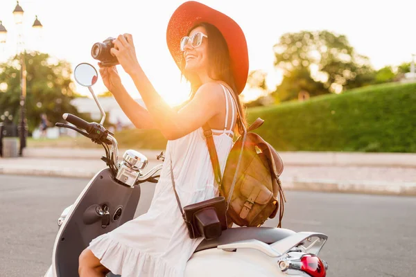 ストリートバイクに乗って魅力的な女性 夏休みのスタイル 楽しみを持っています スタイリッシュな衣装 ヴィンテージ写真カメラで写真を撮る 革のバックパックを身に着けています — ストック写真