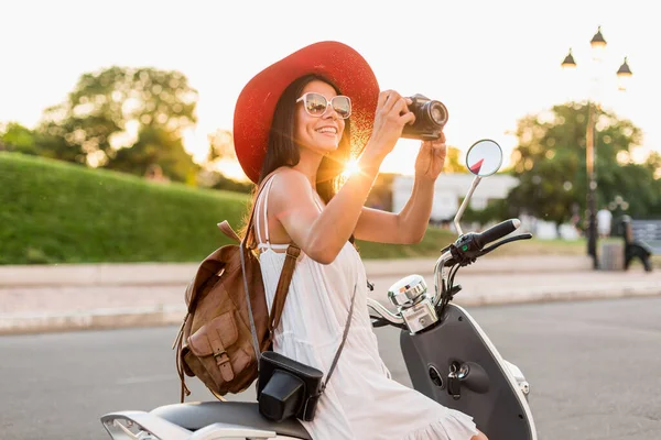 ストリートバイクに乗って魅力的な女性 夏休みのスタイル 楽しみを持っています スタイリッシュな衣装 ヴィンテージ写真カメラで写真を撮る 革のバックパックを身に着けています — ストック写真