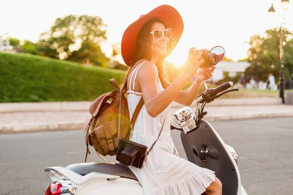 白いドレスを着た夏のスタイルの服装でバイクに乗っている魅力的な笑顔の女性と休暇中に旅行する赤い帽子 ヴィンテージフォトカメラで写真を撮る — ストック写真