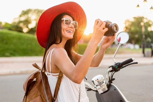ストリートバイクに乗って魅力的な女性 夏休みのスタイル 楽しみを持っています スタイリッシュな衣装 ヴィンテージ写真カメラで写真を撮る 革のバックパックを身に着けています — ストック写真