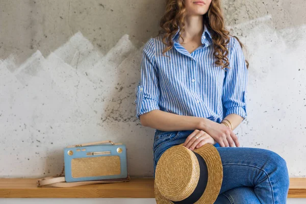 年轻迷人的时髦女人 坐在墙后 手持草帽 手提包 穿着蓝色棉质衬衫 牛仔裤 休闲装 时髦的老式风格 春季夏季时尚潮流 — 图库照片