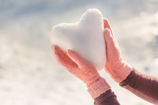 Manos en guantes rosas sosteniendo el corazón de nieve — Foto de Stock