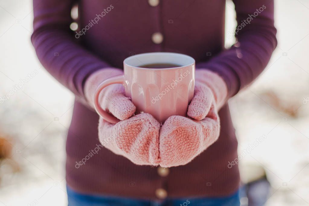 Female hands in pink mittens holding cup with hot tea or coffee. Close up. Winter and Christmas time concept