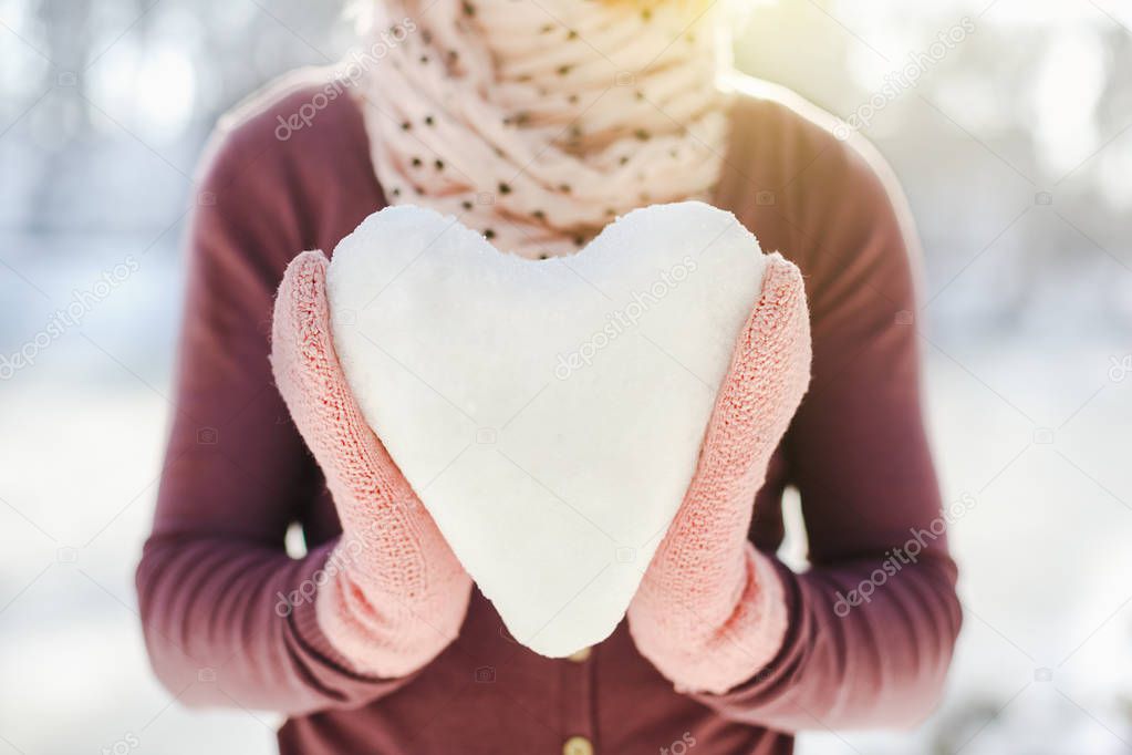 Hands in pink gloves holding snow heart