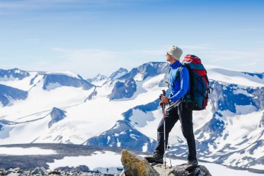 Uzun yürüyüşe çıkan kimse bir dağın tepesinde duran ve tne manzarayı sırt çantası ile