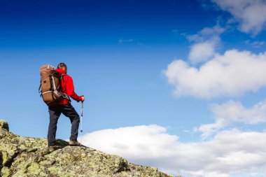 Uzun yürüyüşe çıkan kimse bir dağın tepesinde duran ve tne manzarayı sırt çantası ile