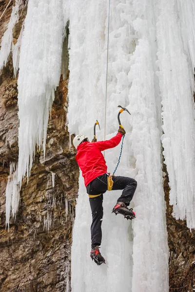 Active man in red coat with white helmet and ice tools climbing an ice wall — Stock Photo, Image