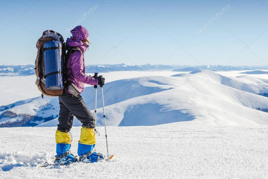 young woman with backpack standing against winter mountain valley - adventure and travel concept