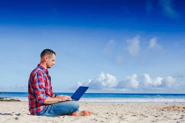 Молодий чоловік з ноутбуком працює на піщаному пляжі — стокове фото