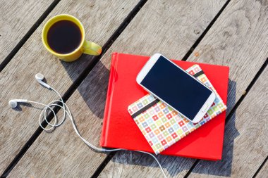 Kahve fincanı, smartphone, kulaklık, ahşap arka plan üzerinde yığılmış kitaplar ile çalışma yer