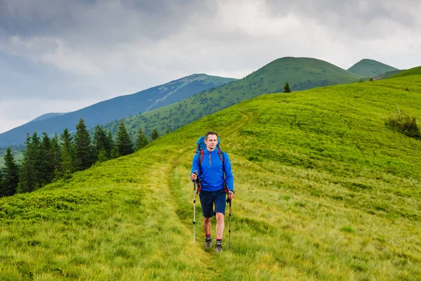 Young man with backpack and trekking poles hiking in the mountains — Stock Photo, Image