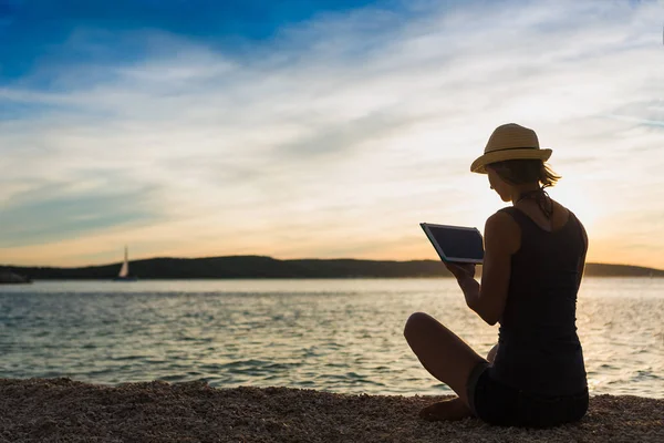 Jovem mulher hipster feliz trabalhando com seu laptop perto do mar ao pôr do sol — Fotografia de Stock