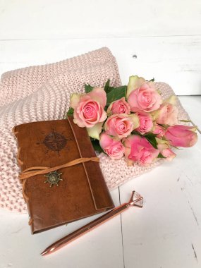 Pembe güller ve pembe battaniye üzerine deri bir defter