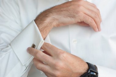 Takım elbisesinin kol düğmesini tamir eden smokinli bir adamın yakın çekimi..