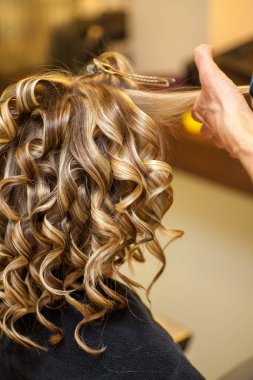 Sarışın bir kadının saçını kıvıran kuaför.
