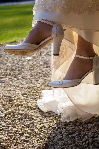 A bride sitting on a chair outside, at the brides feet there are designer high-heeled shoes