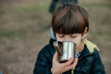 Küçük tatlı çocuk ormanda demir kupadan çay içiyor. 