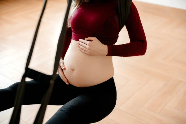 A pregnant woman is doing yoga in studio. She wears tight body. She hugs her baley and is very  carefull with future baby. Concept of mother care, young mother, woman and child, healthy life, fitness.