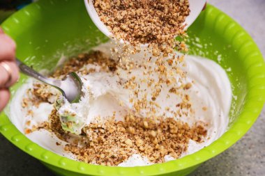 Öğütülmüş ceviz ekşi krema ile bir kase içinde dökülür. Bir pasta için evde bir krem hazırlama süreci gösterilir