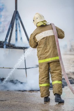 İtfaiyeci, hidrant su ile yardımcı tarafından yangın duman kalıntıları söndürür